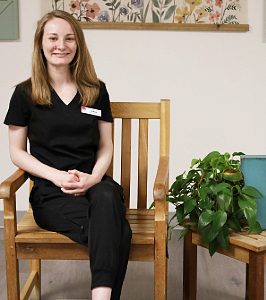Female sitting in chair with hands folded in lap wearing black scrubs