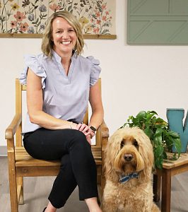 Female sitting in chair next to a large shaggy dog wearing a bow tie